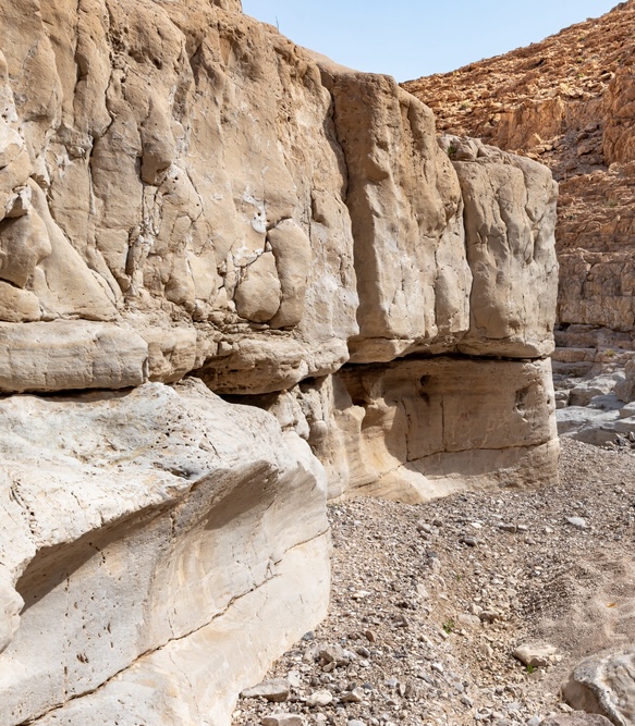 A rocky canyon with no noticable life.  The walls are pale beige.  In the foreground, in a low wall, is a divot suitable to hold a small fountain.

Taken from https://depositphotos.com/photo/dry-river-bed-passing-stone-desert-khatsatson-stream-israeli-side-573814644.html