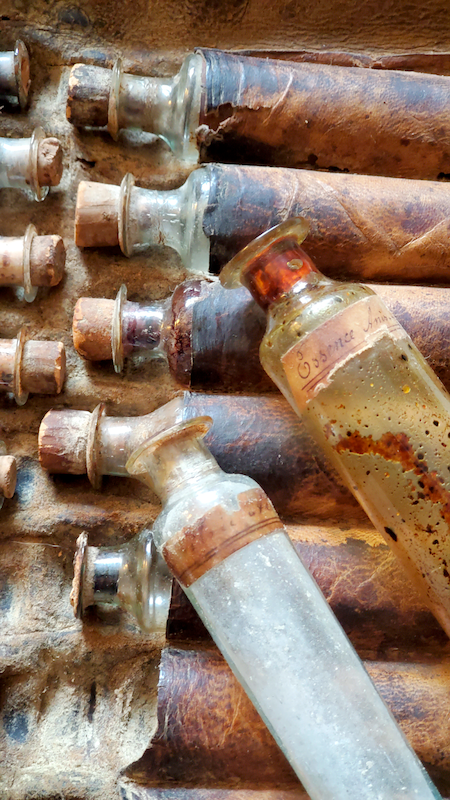 Closeup of a leather roll-up pouch with apothecary vials from the early 19th century.  The corks are worn and the leather is partially blackened with age.  Two bottles are loose and laying diagonal across the image, one has a white powder and the other has a liquid where the colours do not mix.

Taken from http://bottleappraisals.com/product/the-best-early-19th-century-physicians-leather-case-with-original-vials/