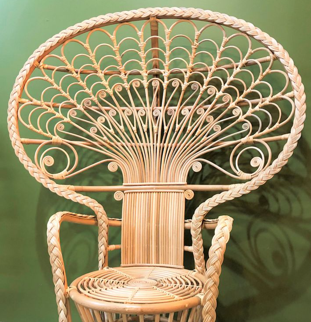 A peacock rattan chair with a green wall behind it