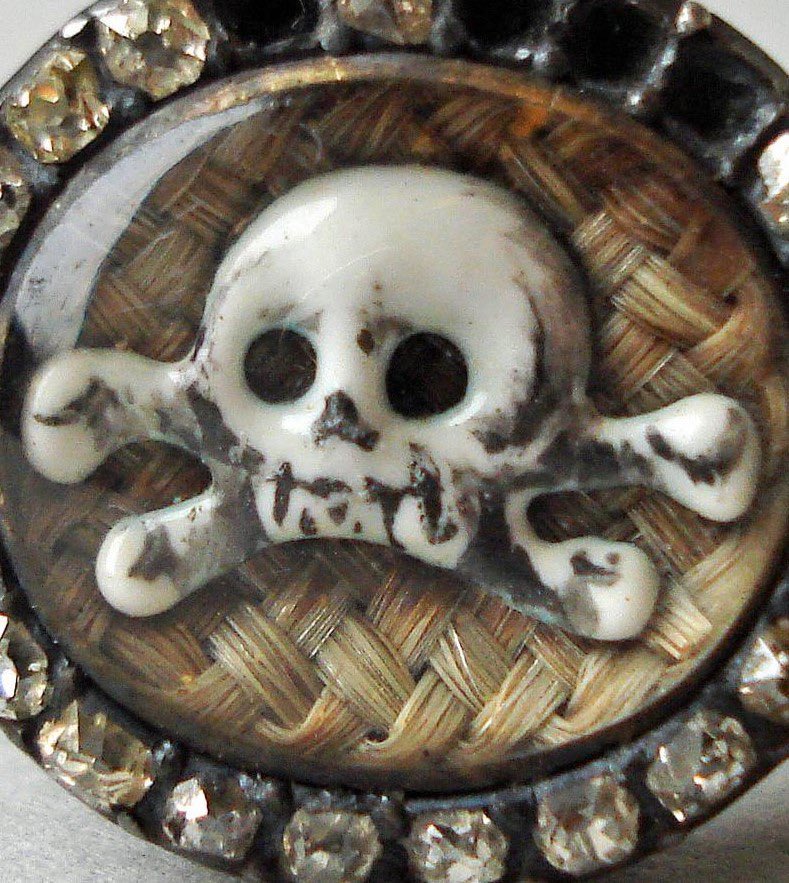 Gold mourning ring with a skull and cross bones on a background of woven hair. The shoulders of the ring are also decorated with a skull and cross bones. 

https://twitter.com/drdan_o/status/1530607836622987273